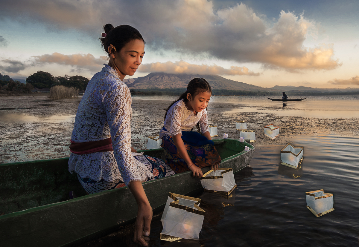 Mom and daughter launch lanterns on the lake on the Festival of the Goddess of Rice in Bali. In front of the volcano Batur.Indonesia
