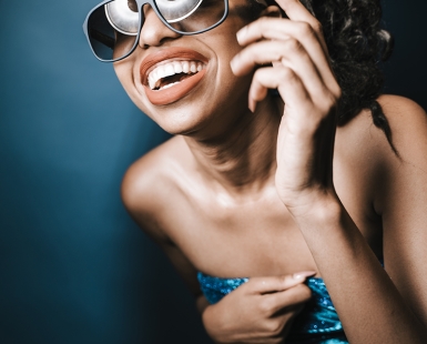 Female model laughing in studio holding onto dress falling off with sunglasses beauty dish reflection